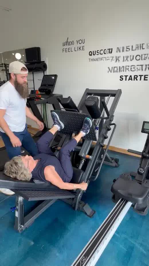 A PEAKFIT. coach guiding a client through a leg press